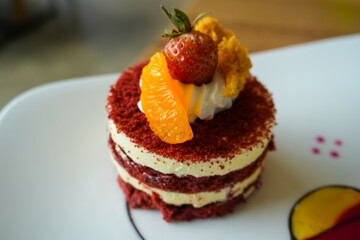 Red velvet cake, classic three layered cake from red butter sponge cakes with cream cheese frosting, with mandarin orange and candied strawberry as topping American cuisine