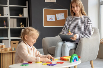 Female psychologist working with little girl doing puzzle in office