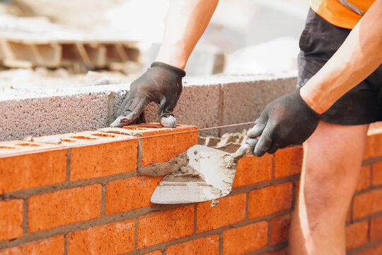 hands of Bricklayer with Masonry Trowel laying bricks on mortar	