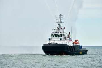 Fireboat ship sails on open sea directing jets of water to sides demonstrating bravery water salute, nautical spectacle of russian maritime strength at Russian naval forces parade