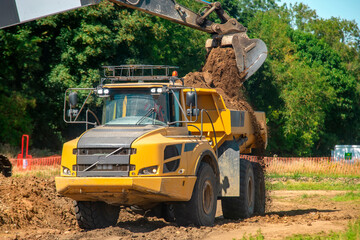 Excavator loading big yellow articulated dump truck earth mover on building site