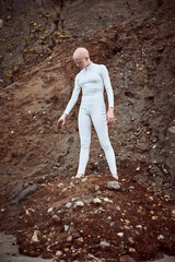 Full length portrait of young hairless girl with alopecia in white futuristic suit holding handful...