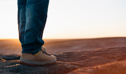 feet of man in travel boots reaching destination on top of mountain at sunrise or sunset. Travel...