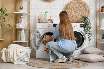 Woman putting clothes into washing machine in laundry room, back view
