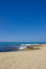 Beach in the South of Italy: sand and rocks, blue water and a blue sky over the horizon