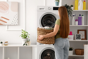 Woman holding wicker basket with clothes in laundry room, back view