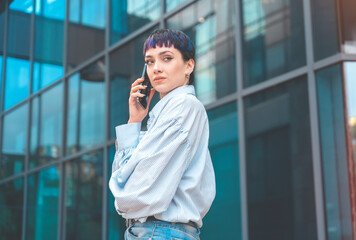 young brunette woman using phone walking past office center toned image