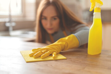 redhead woman in protective gloves and apron cleaning table in kitchen at home