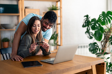 Young happy couple using laptop and credit card while shopping on the internet at home.
