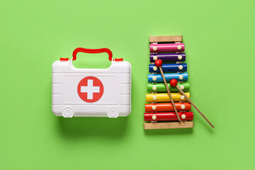 Toy first aid kit with xylophone on green background. Top view