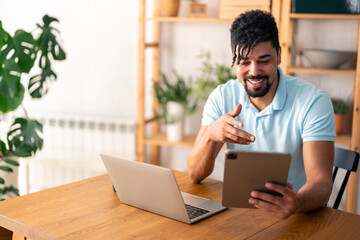 A male business person with beard, dressed in casual clothes is having a video call with his business partners while using his laptop computer for making business plans.