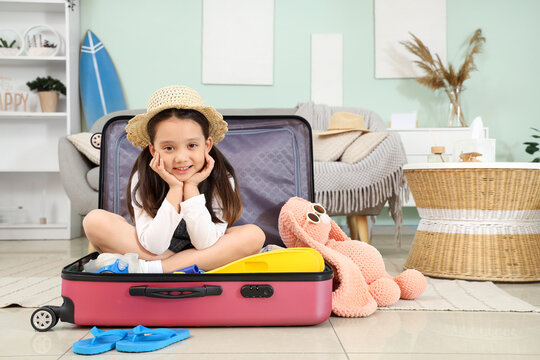 Cute Asian girl sitting on suitcase at home. Travel concept
