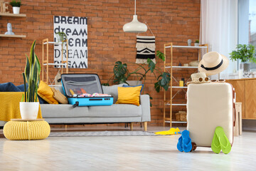 Packed suitcase with hats, sunglasses and flip-flops in living room with traveling accessories....
