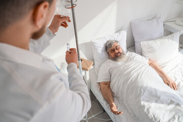 Senior man with drip infusion and caregiver lying in bedroom
