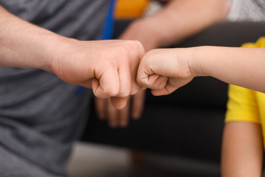 Young man with his little son bumping fists at home, closeup