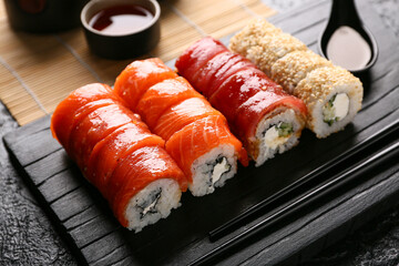Board with tasty sushi rolls and chopsticks on black grunge background, closeup