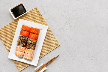 Plate with tasty sushi rolls, chopsticks and soy sauce on grey grunge background