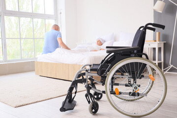 Empty wheelchair of sick mature couple in bedroom