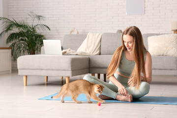 Young woman playing with cute kitten on yoga mat at home