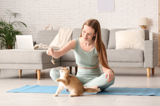 Young woman playing with cute kitten on yoga mat at home