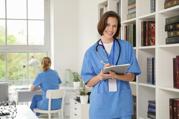 Female medical intern with notebooks near bookshelf in clinic
