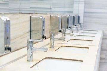 Public bathroom restroom lavatory interior with row of white ceramic sinks, mirrors and faucets