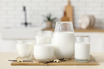 Glasses and jug of fresh vanilla milk with sticks and flowers on table in kitchen