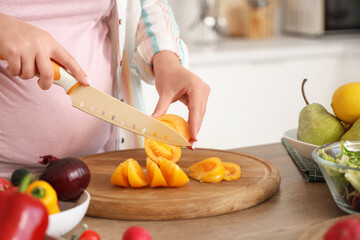 Pregnant woman cutting fresh vegetables for salad in kitchen, closeup