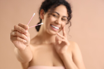 Young African-American woman with cotton buds on beige background, closeup