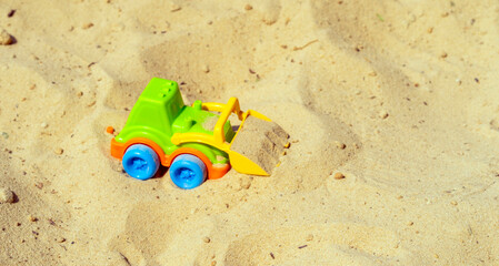 Sand, excavator loads tractor children's toy in sandbox