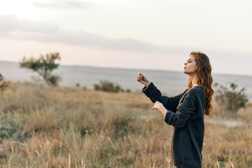 Woman standing in open field with outstretched arms gazing up at the sky in awe