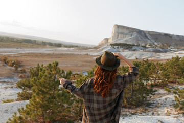 Woman in plaid shirt and hat gazing at majestic mountain view in the distance