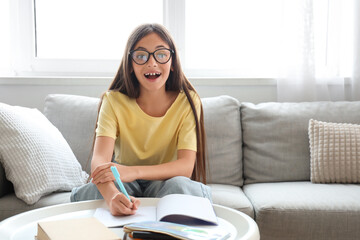 Happy little schoolgirl writing in copybook on sofa at home