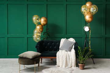 Beautiful golden air balloons with sofa and velvet pouf near green wall at home