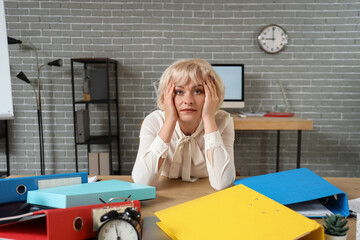 Stressed mature businesswoman sitting at desk in office