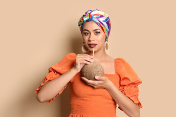 Beautiful African-American woman with fresh coconut on beige background