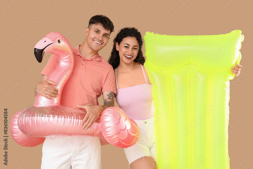 Sticker Happy young couple with inflatable mattress and ring on brown background