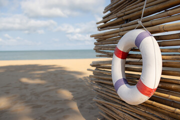A white and red life preserver is hanging from a bamboo fence on a beach. lifebuoy on wooden wall at beach.
