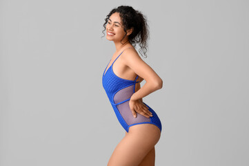 Obraz premium Beautiful young African-American woman in stylish blue swimsuit on grey background