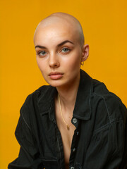 Fototapeta premium Bald young woman with a bright personality. Stylish bald-headed person on yellow background