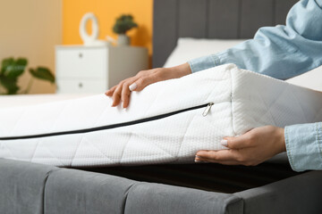 Woman putting soft orthopedic mattress on bed at home, closeup