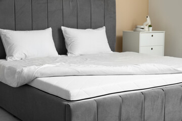 New orthopedic mattress with blanket on stylish bed near beige wall in room, closeup