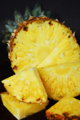 Ripe juicy pineapple next to cut pieces on a wooden board on a dark background