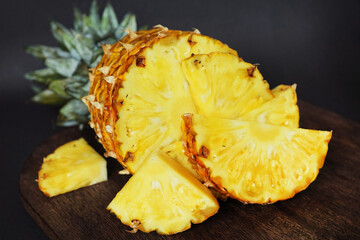 Ripe juicy pineapple next to cut pieces on a wooden board on a dark background