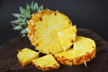 Ripe juicy pineapple next to cut pieces on a wooden board on a dark background