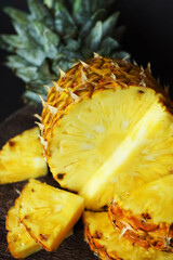 Ripe juicy pineapple next to cut pieces on a wooden board on a dark background