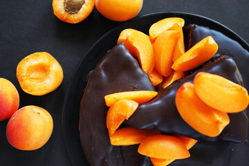 Chocolate cake with chocolate icing and fresh apricots on a dark background