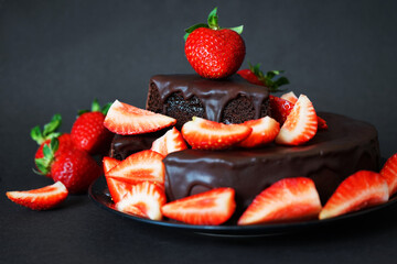 Chocolate cake with chocolate icing and fresh strawberries on a dark background