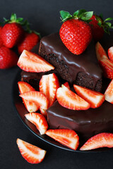 Chocolate cake with chocolate icing and fresh strawberries on a dark background
