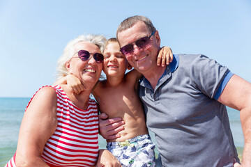 An elderly man and woman hugging a boy on the seashore on a sunny day. Love and tenderness. Happy...